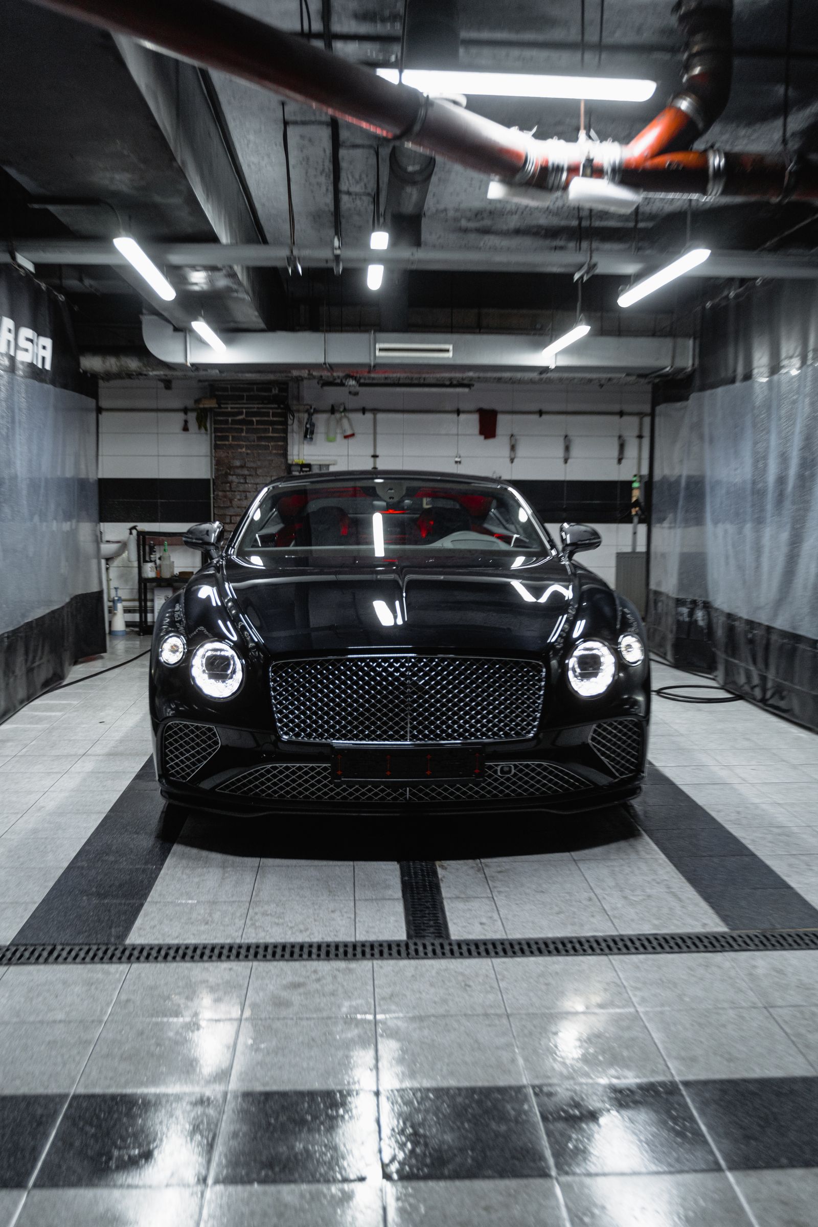 Black luxury coupe parked in a dark garage bay with a glossy, mirror-like floor finish